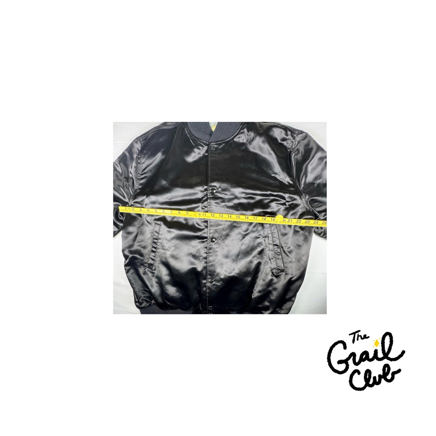 Black satin jacket with a measuring tape around it on a white background, branded 'The Grail Club'.