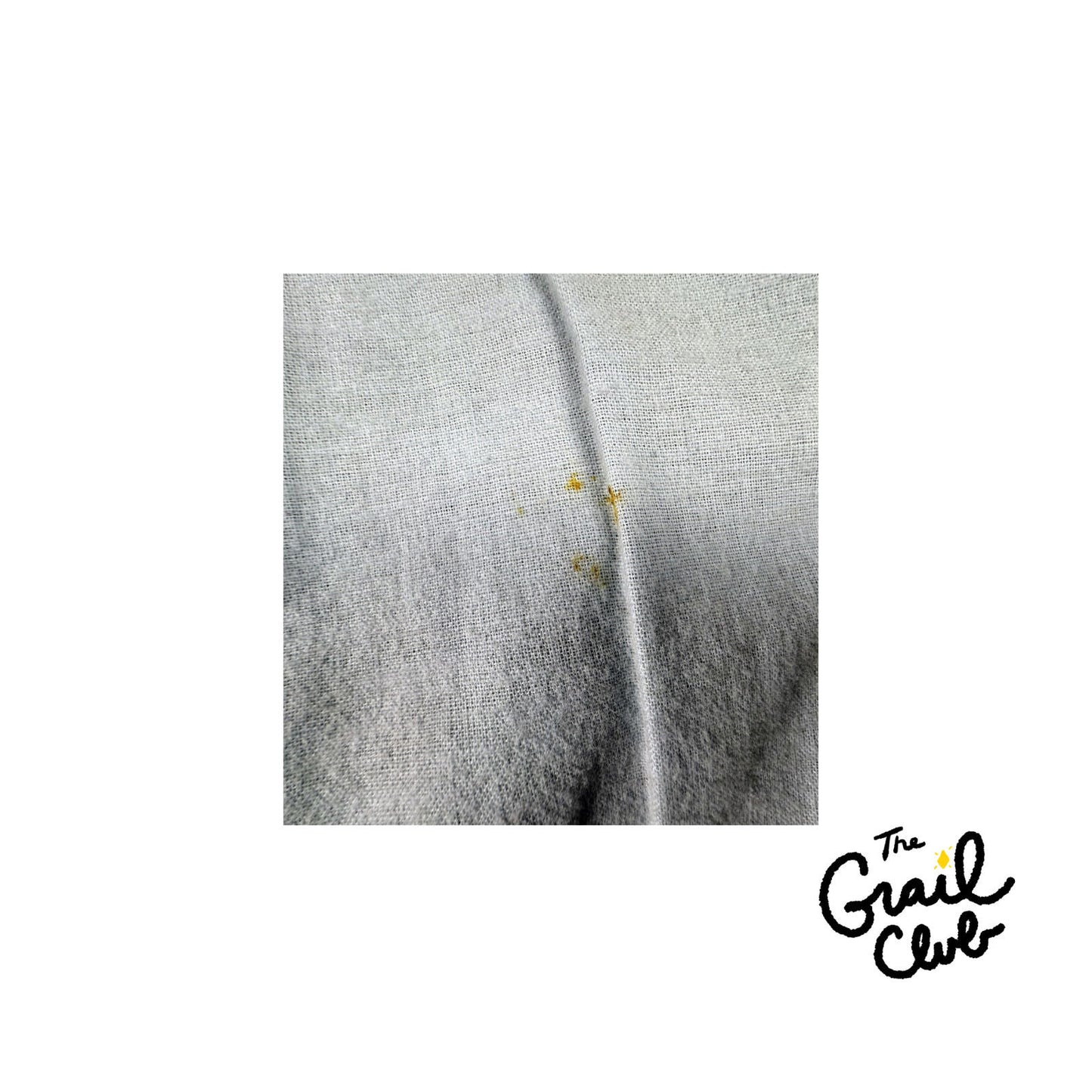 Close-up of a gray fabric with yellow stains on a white background, featuring 'The Grail Club' logo.
