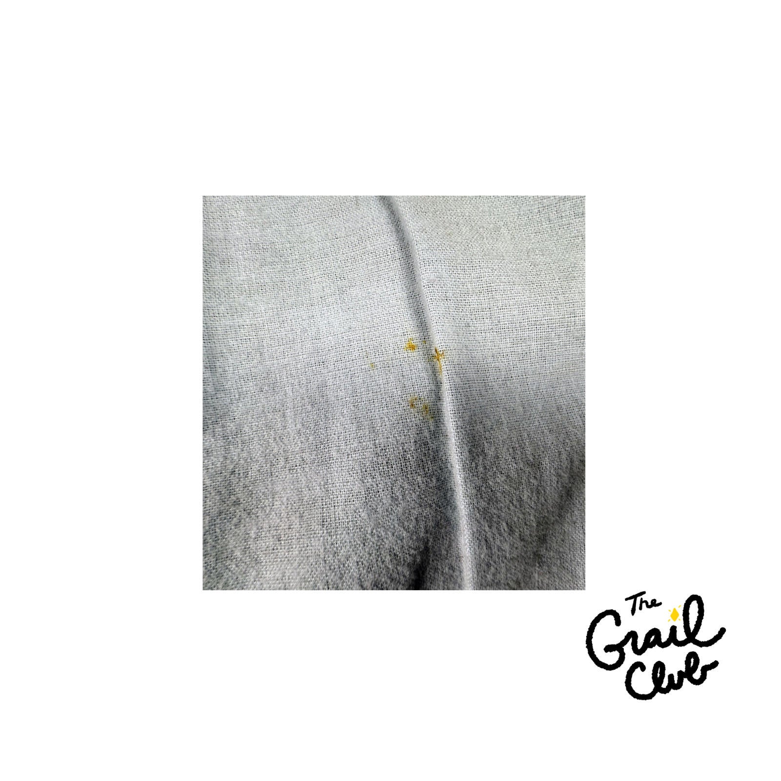 Close-up of a gray fabric with yellow stains on a white background, featuring 'The Grail Club' logo.